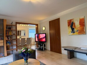 A living room with a television, a bookshelf, a dining area, and a painting on the wall. - Ferienhaus Winterberg (Winterberg)
