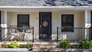 A two-story house with a front porch, a black door with a logo, and two windows with shutters.