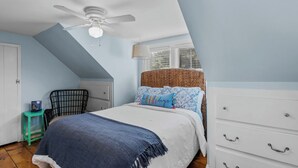 A bedroom with a bed, a ceiling fan, a window, a chair, and a dresser.