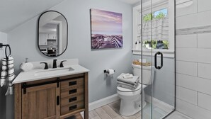 A modern bathroom with a wooden vanity, a glass shower enclosure, and a view of the outdoors through a window.