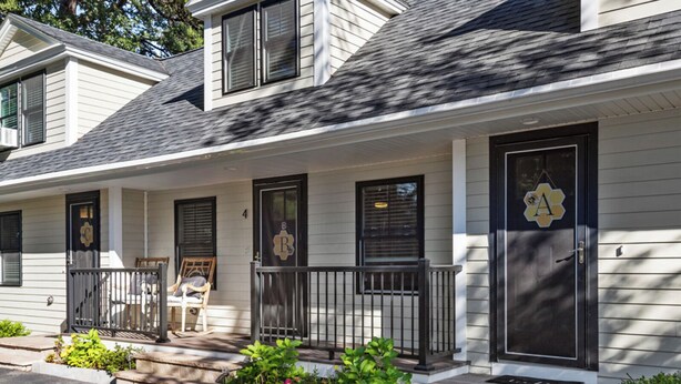 A two-story house with a front porch, a black door with a yellow emblem, and a small garden area.