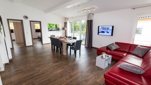 Ein modernes Wohnzimmer mit einem roten Sofa, einem Esstisch mit Stühlen und einem an der Wand befestigten Fernseher.