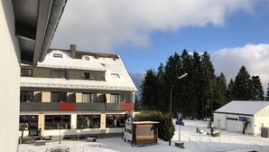 Ein mehrgeschossiges Gebäude mit verschneitem Gelände, einem Parkplatz und einem Wald im Hintergrund.