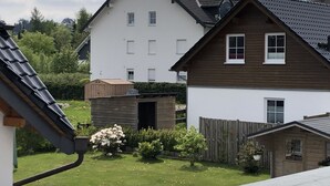 Ein Wohngebiet mit einem zweigeschossigen Haus, einem Holzschuppen und einem eingezäunten Garten.