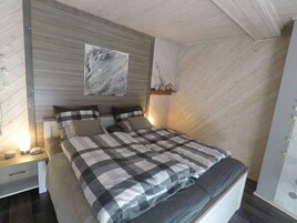 Quarto com cama, mesa de cabeceira, prateleira na parede e um quadro.