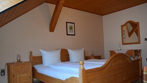 A wooden bed in a room with a sloped ceiling, a nightstand, a bedside table, and a mirror on the wall. - Ferienhaus Herzog (Haundorf)