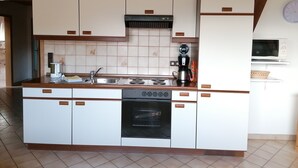 A kitchen with white cabinets, a stove, an oven, a microwave, and a coffee maker. - Ferienhaus Herzog (Haundorf)