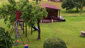A rustic cabin with a porch and a swing set in a grassy area with trees. - Ferienhaus Herzog (Haundorf)