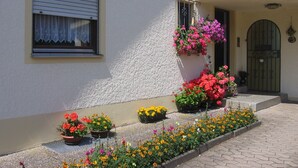 A building with a window with a white curtain, a door with a green gate, and various flower pots with colorful flowers. - Ferienhaus Herzog (Haundorf)