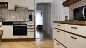 A kitchen with wooden cabinets, a built-in oven, and a microwave. - Ferienhaus Betty (Selbitz)