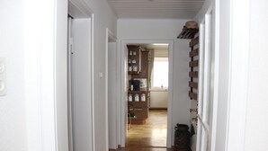A narrow hallway with wooden flooring, white walls, and a door leading to a room with a radiator and shelves. - Ferienhaus Betty (Selbitz)