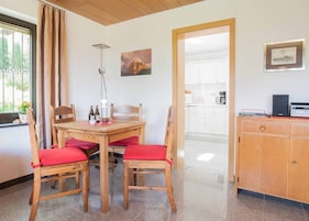 Un comedor con una mesa y sillas de madera, una lámpara y vistas a una cocina.