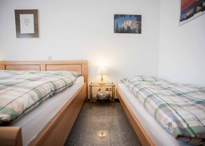 Ein Doppelzimmer mit zwei Betten, einem Nachttisch mit Lampe und gerahmten Bildern an der Wand.