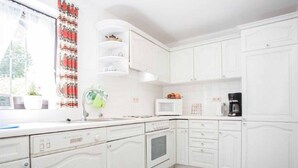Una cocina con armarios blancos, microondas, cafetera y ventana con cortina.