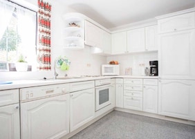 Una cocina con armarios blancos, microondas, cafetera y ventana con cortina.