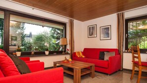 Una sala de estar moderna con muebles rojos, una mesa de centro de madera y ventanas amplias con cortinas.