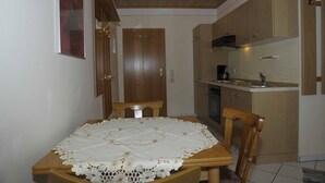 A compact kitchen with wooden cabinets, a dining table with a lace tablecloth, and a wooden ceiling. - Ferienwohnungen Lehner (Mitteleschenbach)