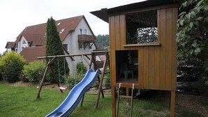 A wooden playhouse with a slide, a swing set, and a small green chair. - Ferienwohnungen Lehner (Mitteleschenbach)