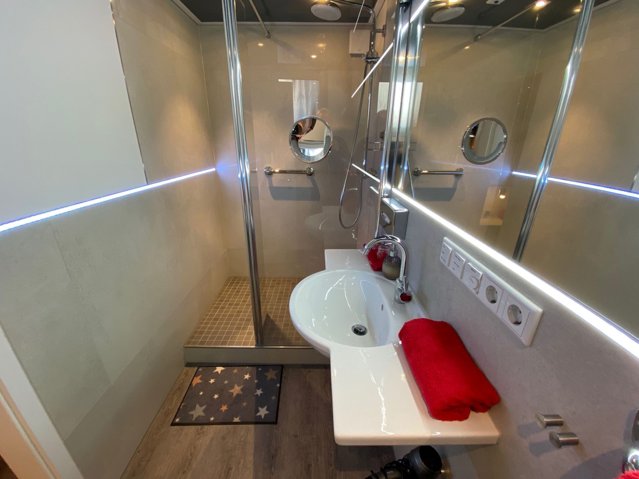 Un baño moderno con ducha de vidrio, lavamanos blanco y toalla roja.