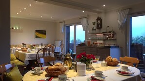 Un comedor con mesas redondas dispuestas para el desayuno, que incluye pan, pasteles y flores.