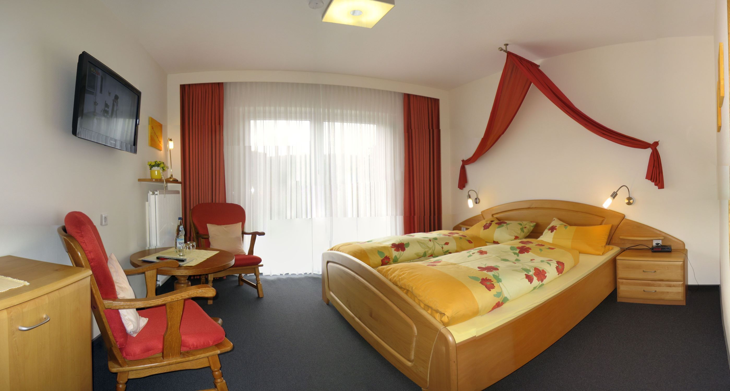 A hotel room with a bed, a desk, a chair, a TV, and a window with curtains.