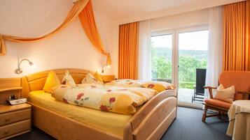 Habitación de hotel con una cama grande, una mesita de noche de madera, una silla y vistas a zonas verdes por la ventana.