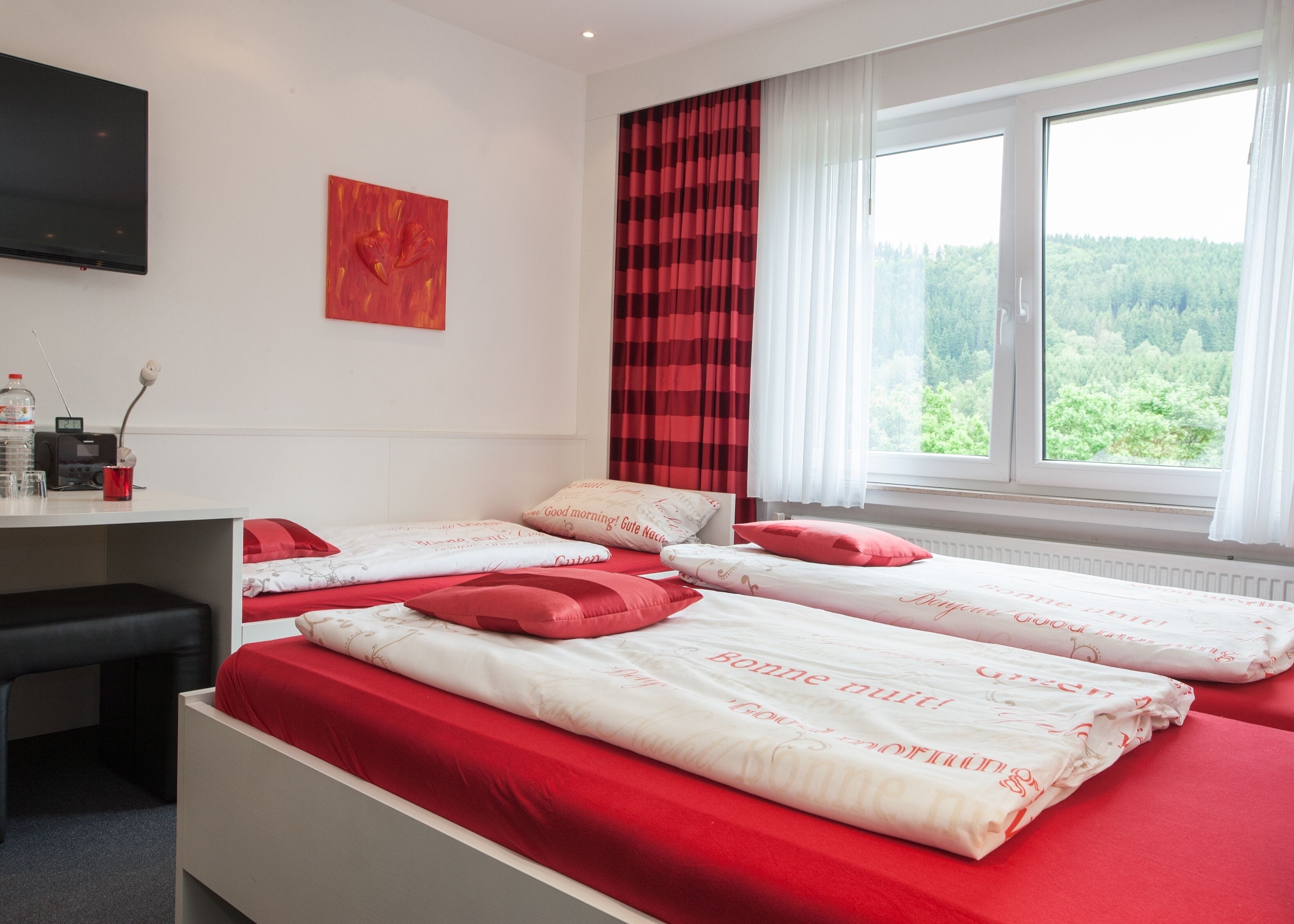 Habitación de hotel con dos camas, un escritorio con una radio y una ventana con vistas al bosque.