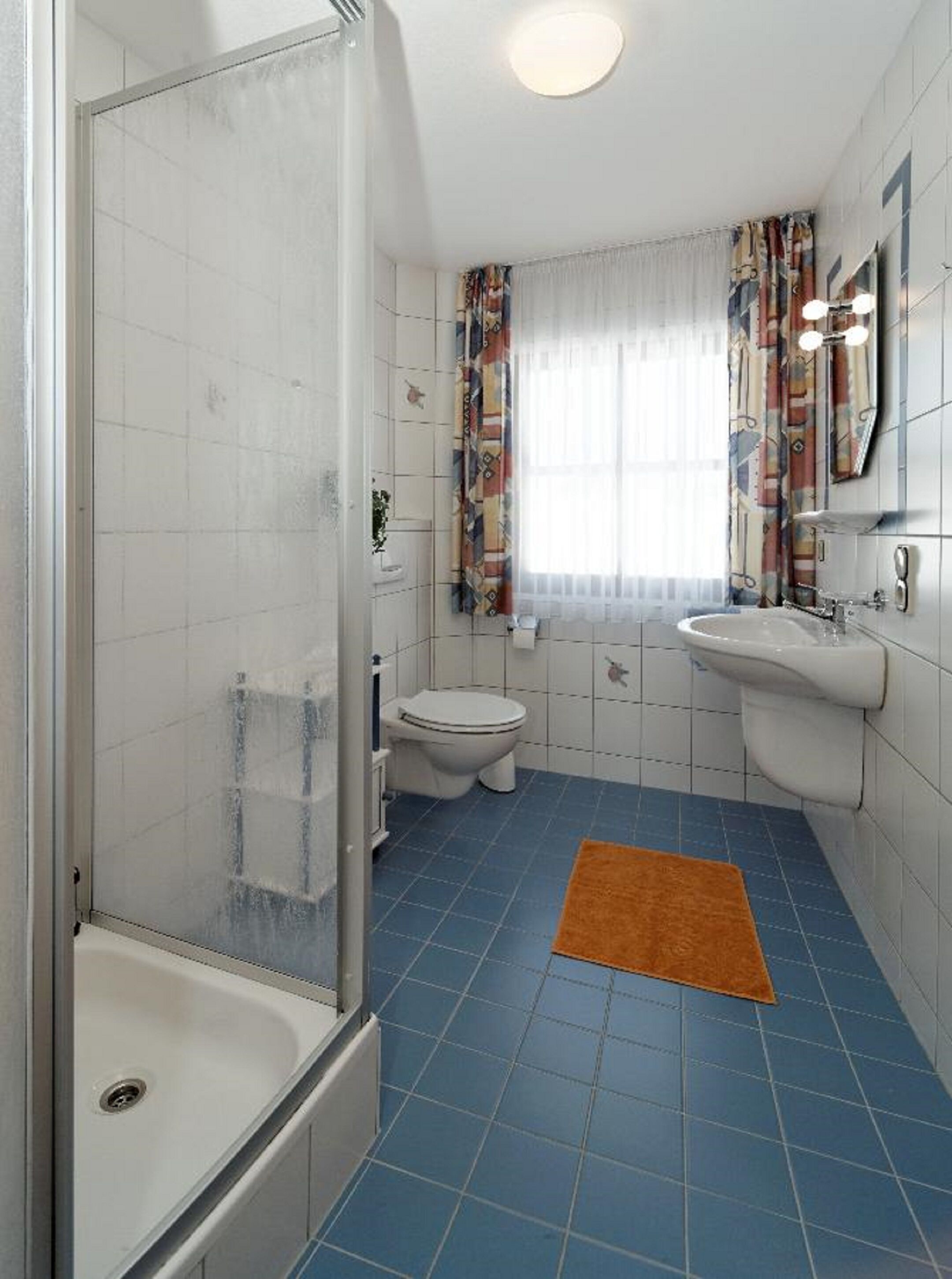 Un baño con ducha, inodoro, lavamanos y piso de baldosas azules.