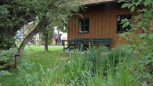 Una cabaña de madera con un banco y una mesa, rodeada de exuberante vegetación y un árbol.