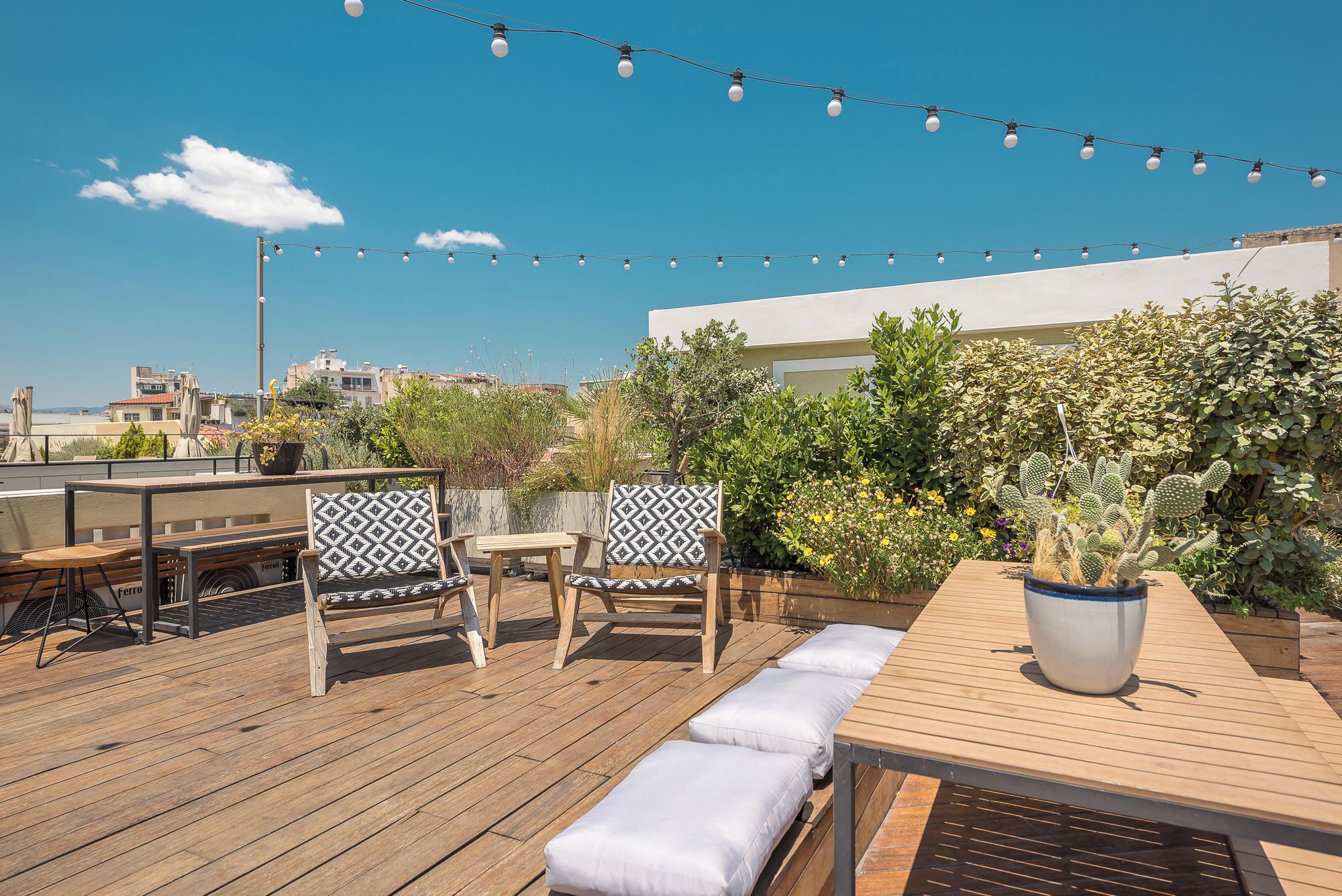 Une terrasse sur le toit, aménagée avec des meubles en bois, des guirlandes lumineuses et un cactus.
