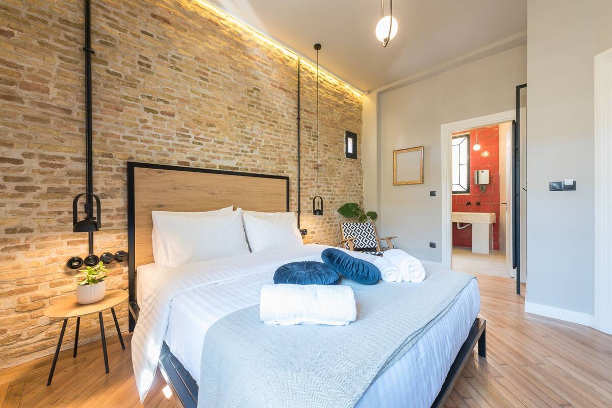 A modern bedroom with a brick wall, a wooden bed frame, and a small bedside table with a plant.