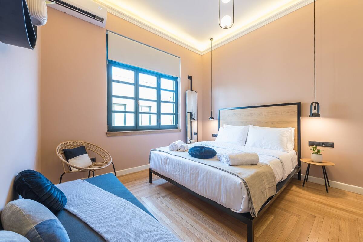 A modern bedroom with a bed, a chair, a bedside table, and a window.