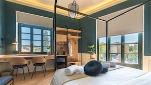 Une chambre avec un grand lit, un bureau et une chaise. Il y a une fenêtre donnant sur les bâtiments à l’extérieur.
