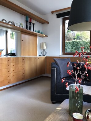 A modern kitchen with wooden cabinets, a dining area with a table, and a window with a view of greenery. - Ferienwohnungen Am Forsthaus (Schonungen)