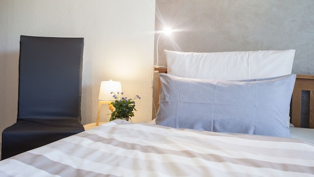 A hotel room with a bed, a chair, a nightstand with a lamp, and a small plant. - Ferienwohnung Mia (Winterberg)