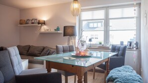 A modern living room with a glass-top dining table, grey sofas, and a wooden floor. - Ferienwohnung Mia (Winterberg)
