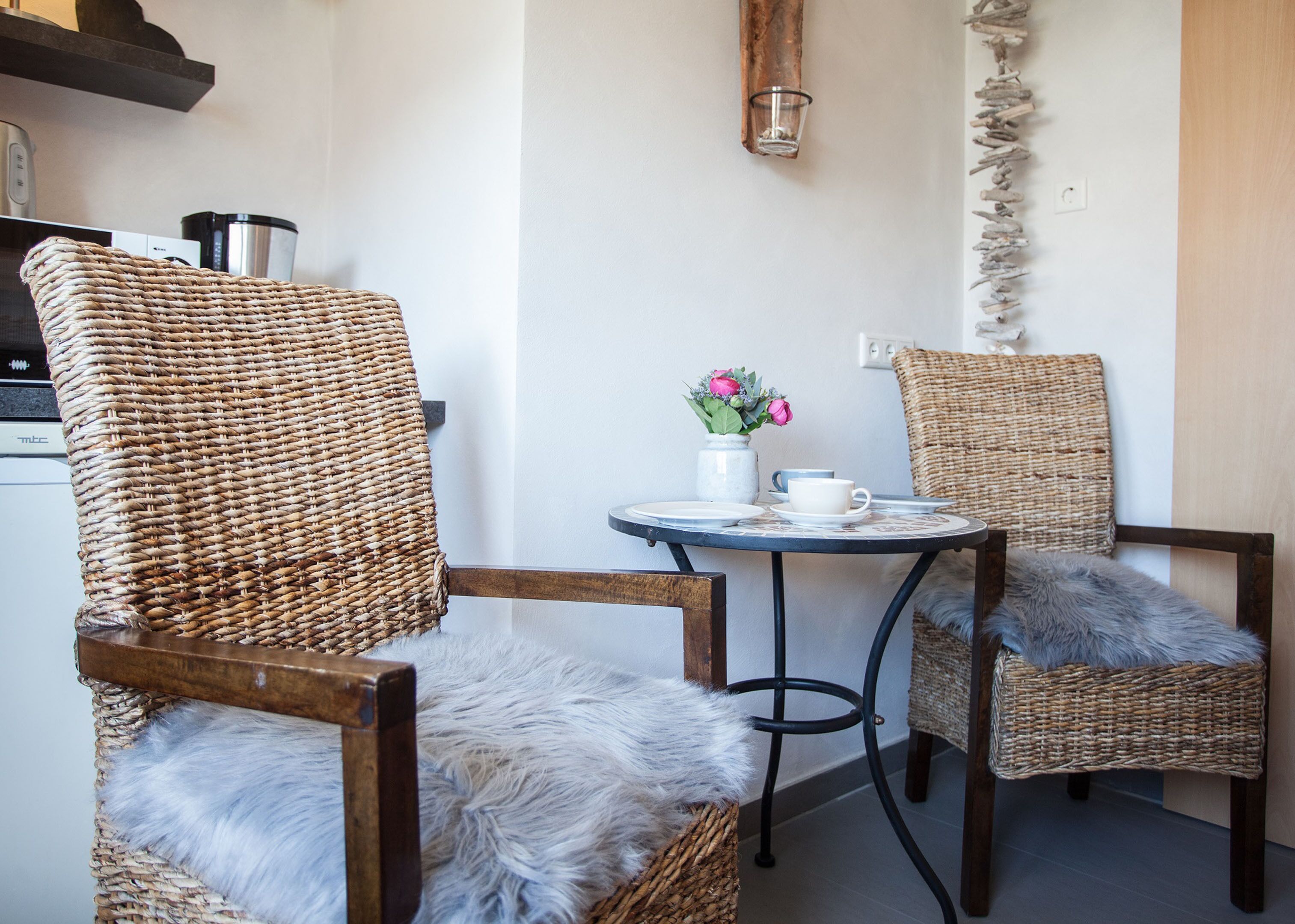 A cozy seating area with wicker chairs and a small round table, featuring a vase with flowers and a cup.