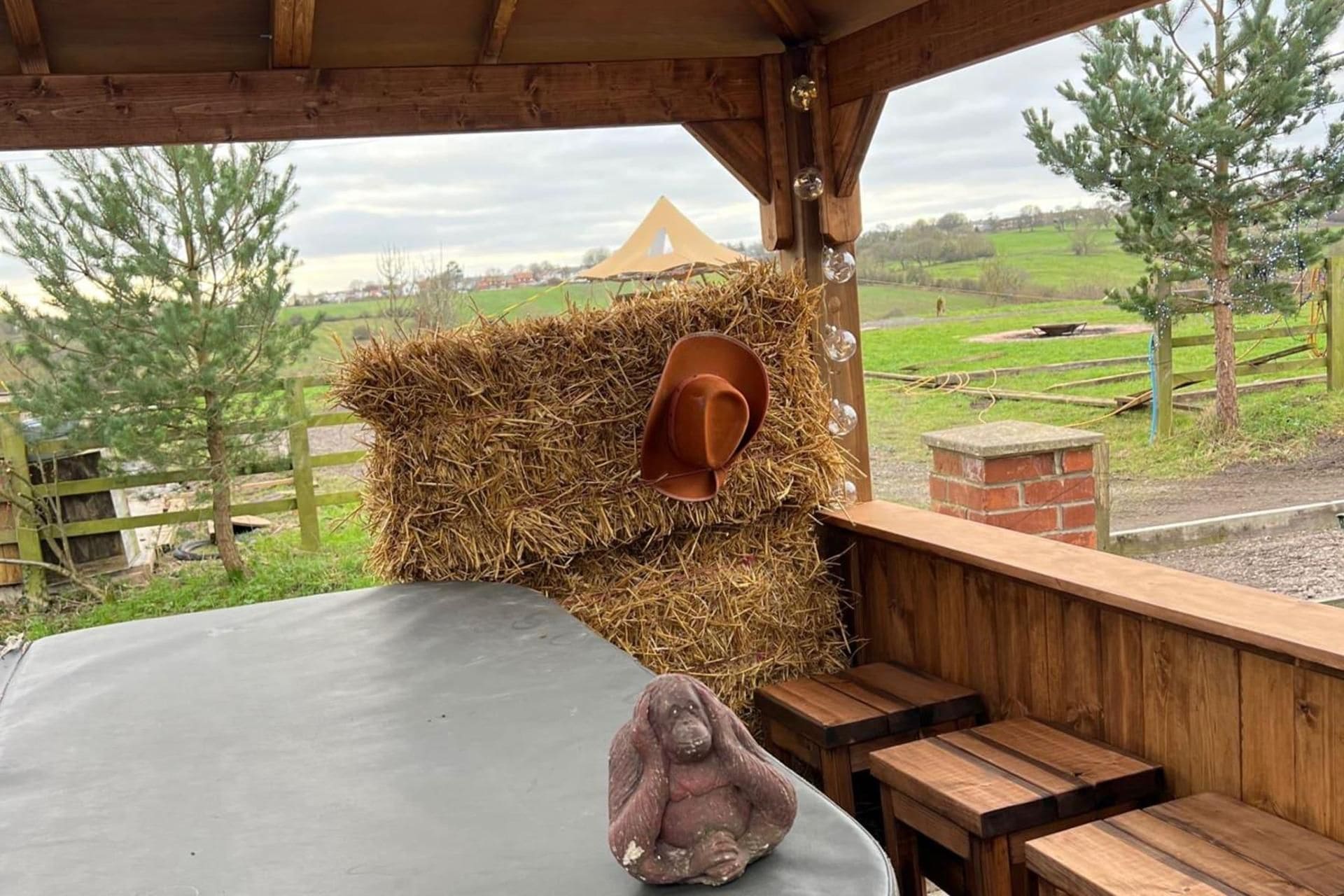 Un espace extérieur rustique aménagé avec des places assises, comprenant une botte de foin, une table en bois et un banc.