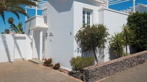 Una villa blanca con un muro de piedra, una pérgola y una palmera.