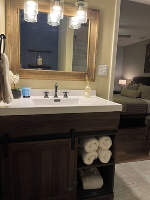 A bathroom with a wooden vanity, a mirror, and a sink. There are towels stored in a wooden cabinet below the vanity.