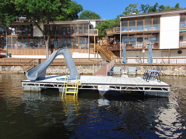 A dock with a slide, a small deck with chairs, and a sign with an address.