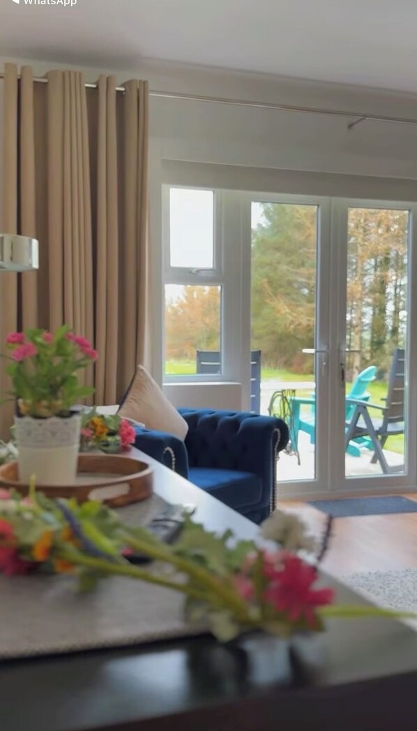 A living room with a blue sofa, a coffee table with flowers, and a view of outdoor patio chairs through a glass door.
