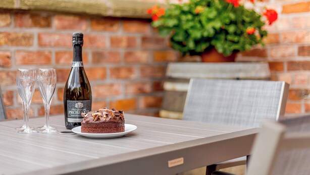 A table with a bottle of champagne, two glasses, and a slice of cake. - Tadpole Cottage at Frog Hall (Tilston, near Malpas)