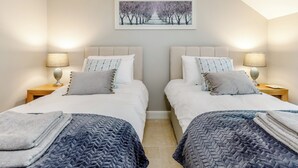 A bedroom with two beds, each with a nightstand and lamp, a painting above the beds, and a view of the hallway. - Tadpole Cottage at Frog Hall (Tilston, near Malpas)
