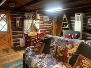Cozy cabin-style room with a wooden dining table, patterned sofa, and green armchair, offering a comfortable atmosphere.