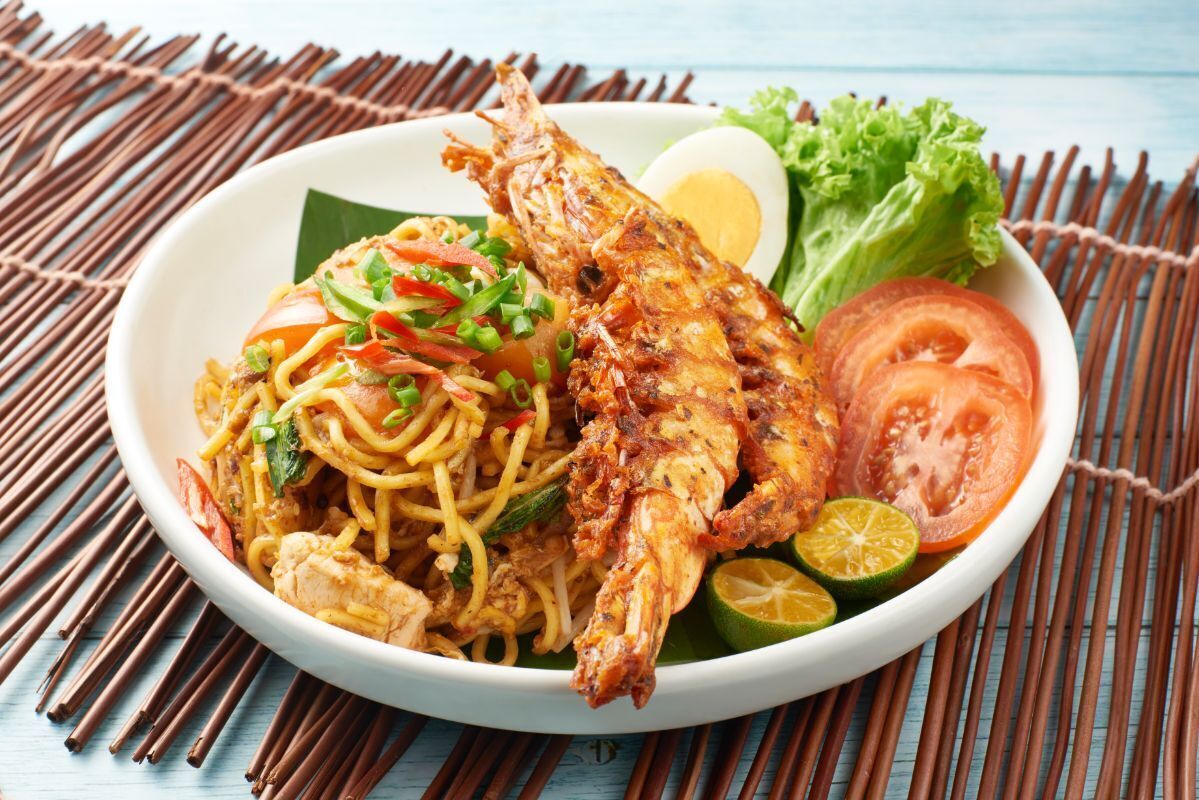 A bowl of noodles with fried fish, boiled egg, and fresh vegetables.