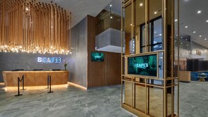 A reception area with a wooden reception desk, a hanging light fixture, and a digital screen displaying 'SCAPES'. - SCAPES Hotel (Genting Highlands)
