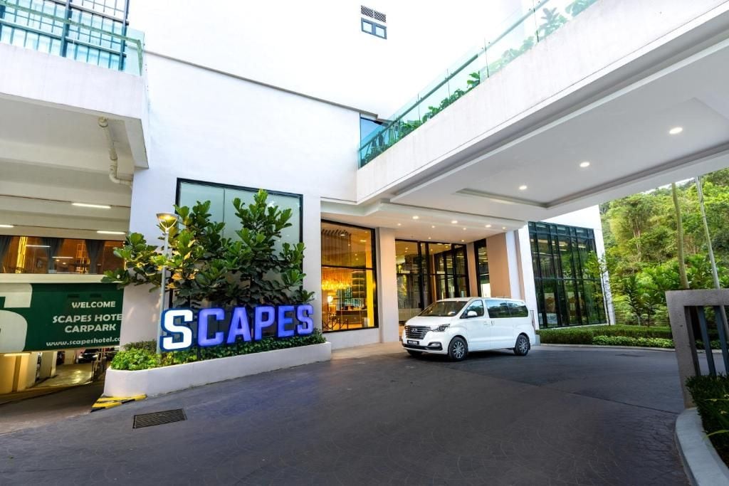 L’entrée d’un hôtel, avec une grande enseigne indiquant « PARC DE STATIONNEMENT DE L’HÔTEL SCAPES », et une voiture blanche garée devant.