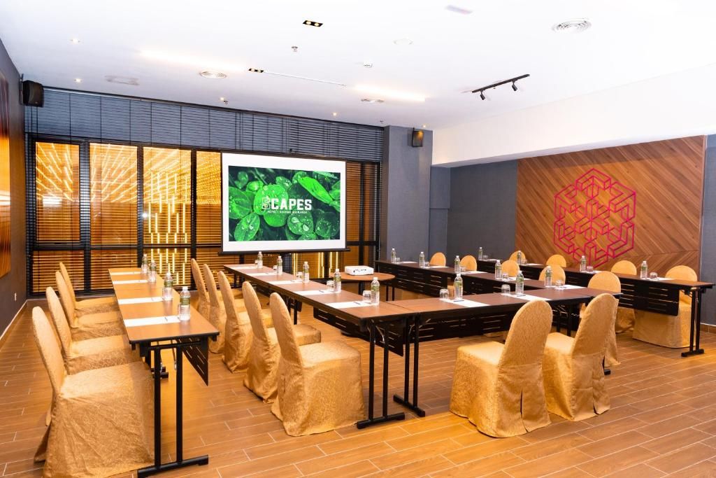 A conference room with tables and chairs, a large screen displaying 'CAPES', and a geometric wall design.