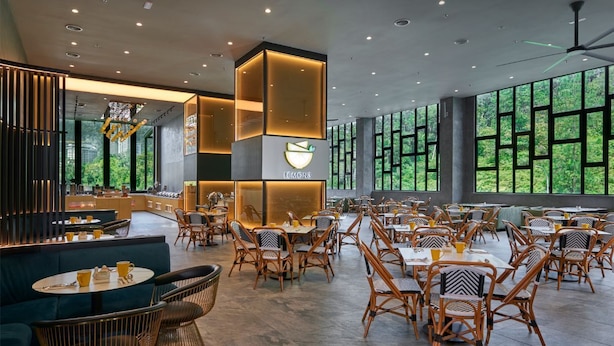 A modern restaurant with a central 'LEMON' sign, surrounded by wicker chairs and tables, with large windows offering a view of greenery. - SCAPES Hotel (Genting Highlands)